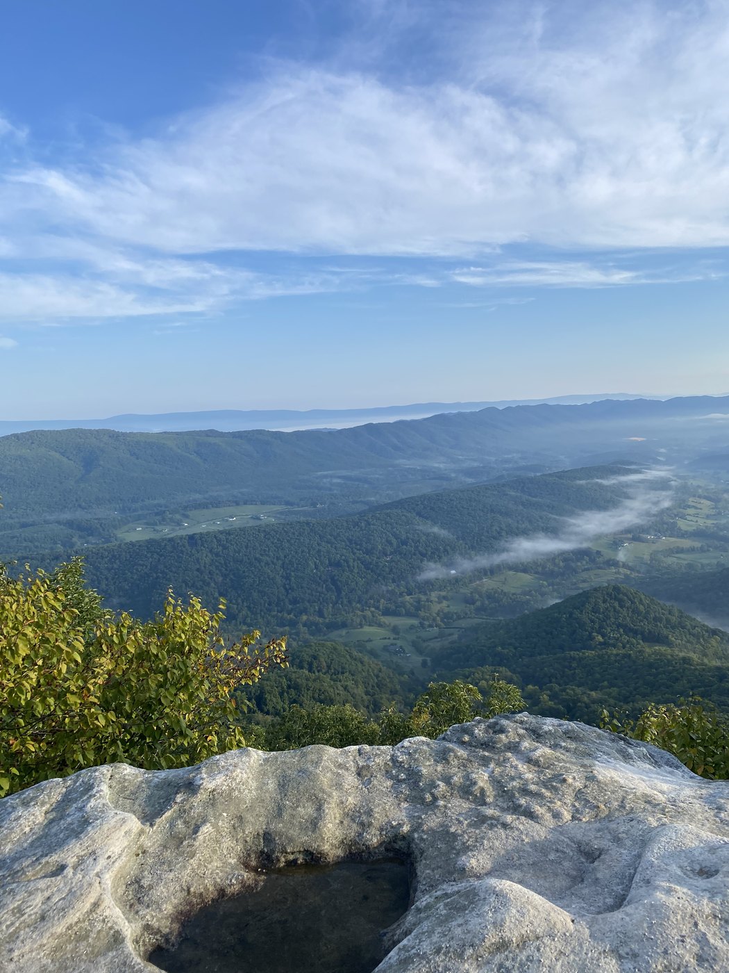 Bare rock foreground opening onto a hazy valley at sunrise