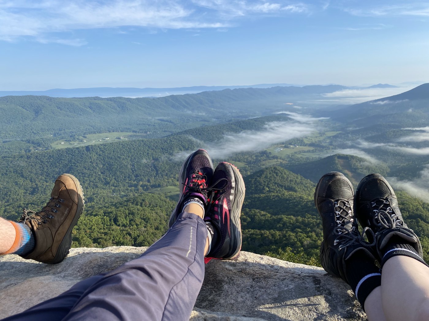 Boots resting on rock at a summit, layered blue ridges and low cloud beyond
