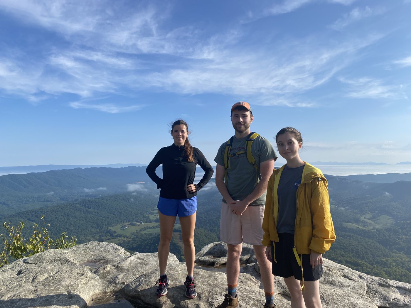 Three hikers standing on a rocky summit above a ridgeline