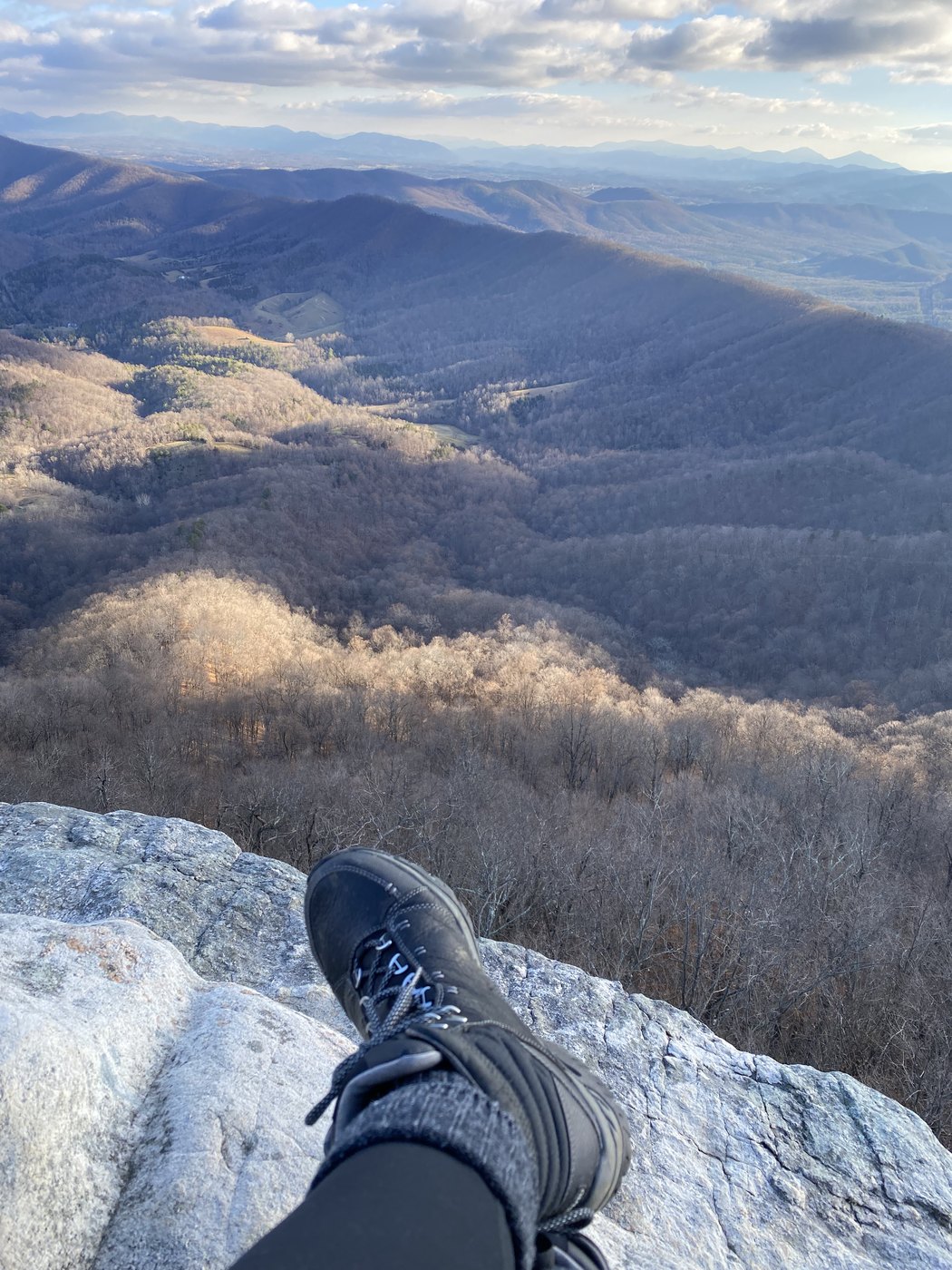 Hiking boots on a summit ledge above a wooded valley