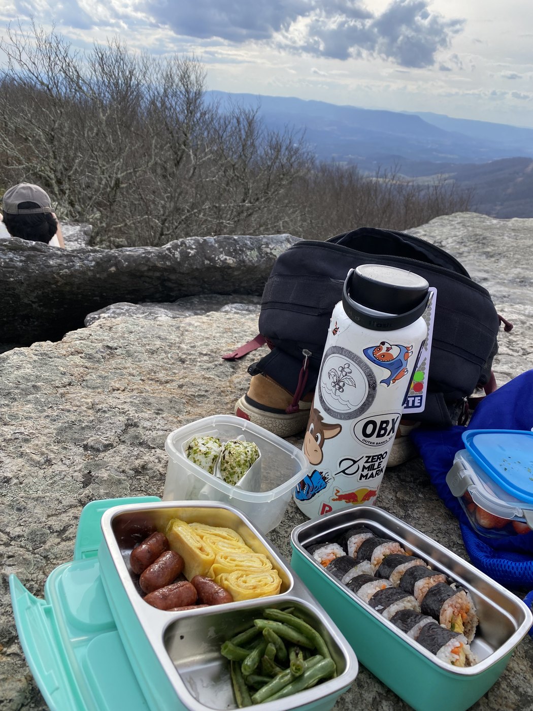 Packed lunch boxes and a flask spread out on rock at a viewpoint