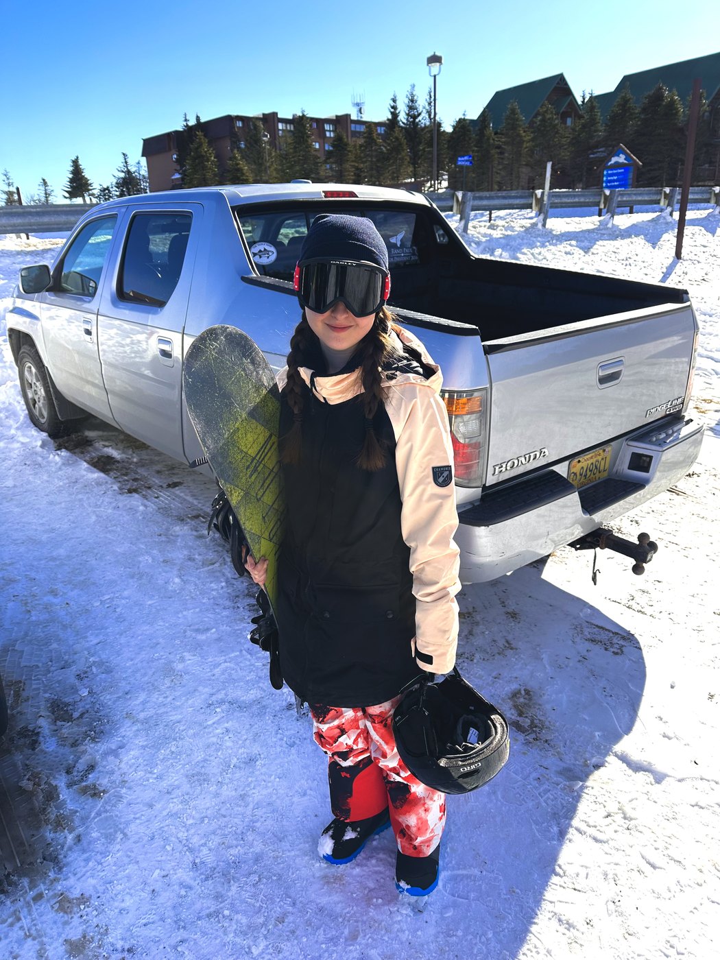 Madeline in snowboard gear beside a pickup truck in a snowy parking lot