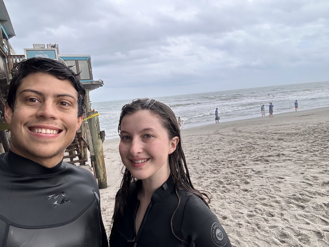 Two people in wetsuits on the beach after surfing