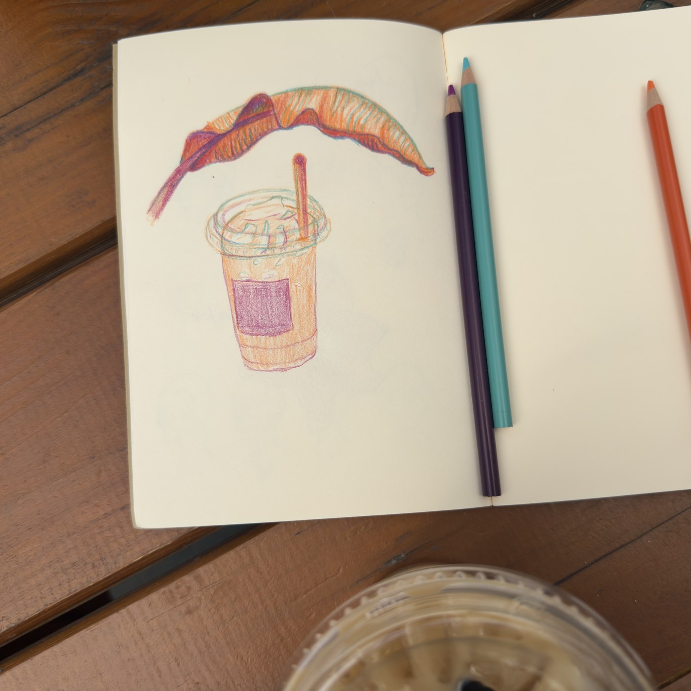 Colored pencil sketchbook drawing of an iced coffee, pencils resting on the open page