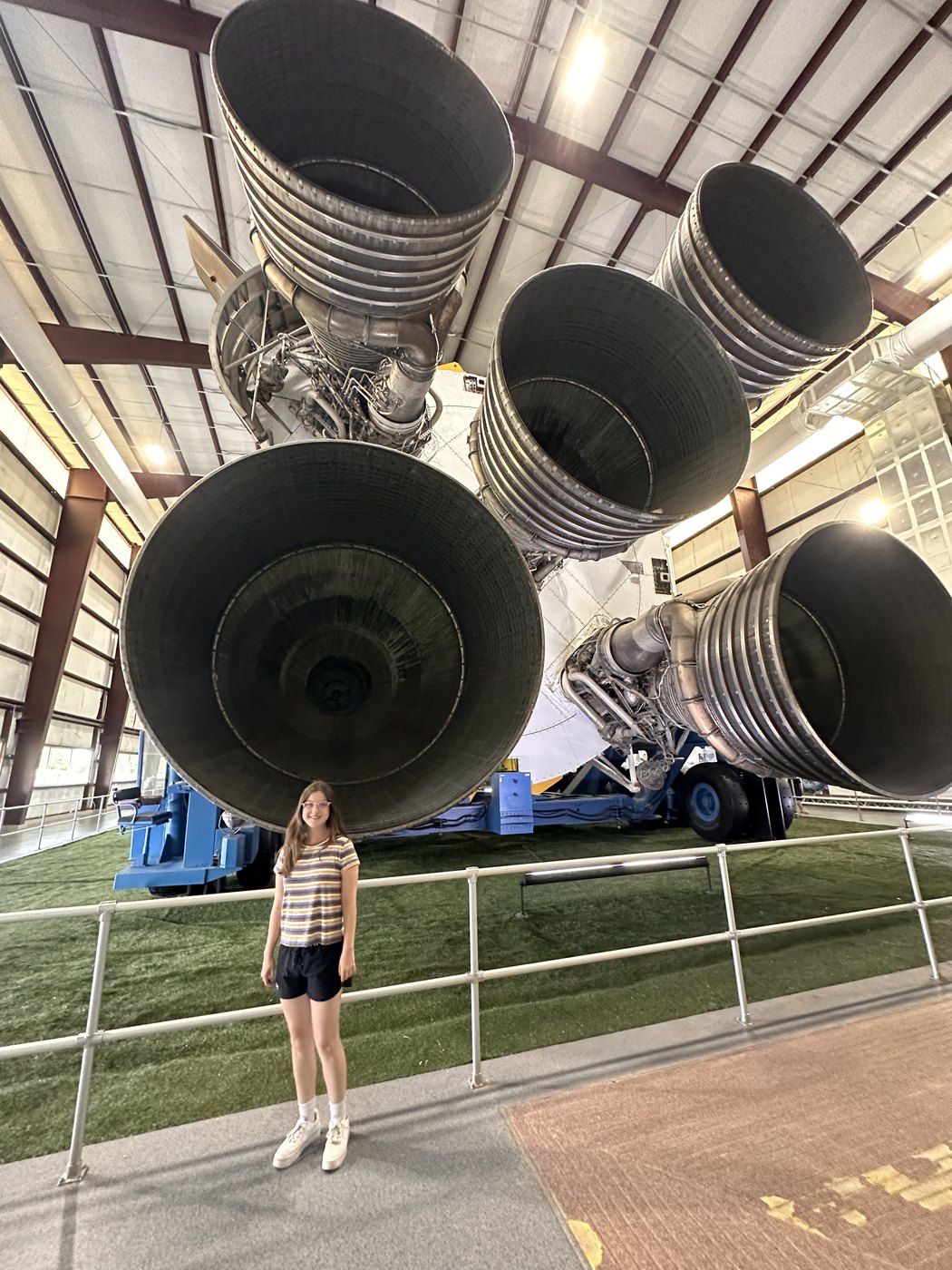 Madeline standing beneath the five F-1 engine nozzles of a Saturn V at Space Center Houston